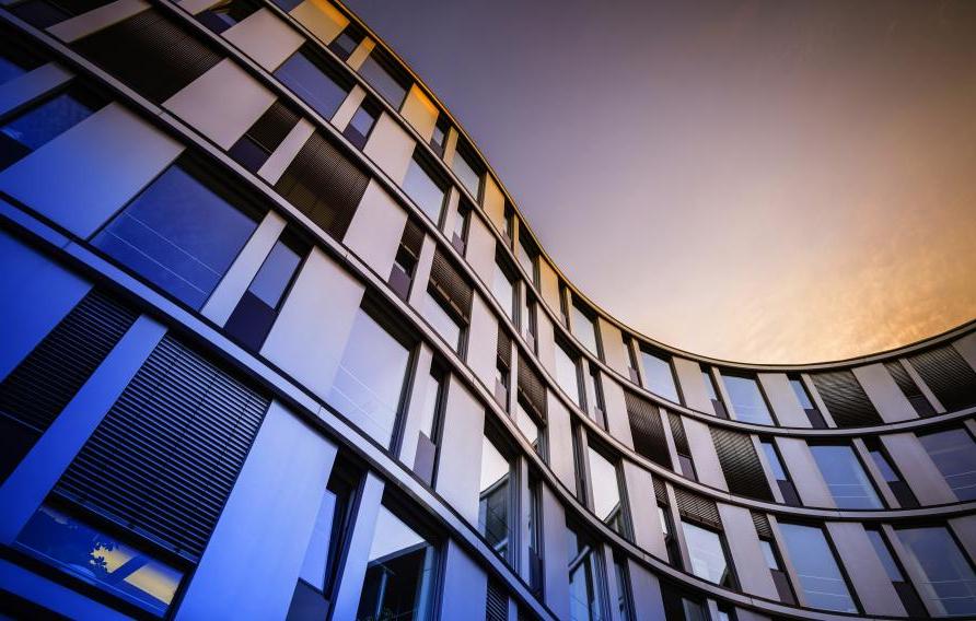 Curved office building with many windoes shaded in multi-colored sky